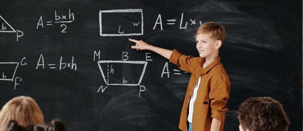 maths_person Boy pointing at a blackboard with maths and shapes on it.